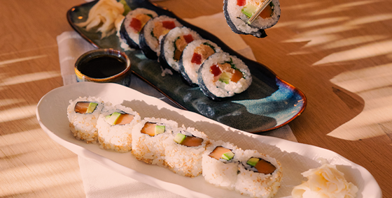 Fresh raw SalmOnderful sushi platter served at OLALA! restaurant with assorted California and tuna rolls garnished with pickled ginger and wasabi, set against a backdrop of elegant candles on a wooden table