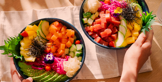 Delectable vegan poké bowls by OLALA! featuring the fish-free delights, Raw TunaliciOus and Raw SalmOnderful, as centerpiece alternatives. These vibrant, veggie-packed creations, garnished with edible flowers and sesame seeds, embody the spirit of ‘oh lala’ in every bite. Perfect for those seeking plant-based, seafood alternatives, the dishes are showcased in a serene setting with candles, symbolizing OLALA!'s commitment to vegan and vegetarian culinary innovation